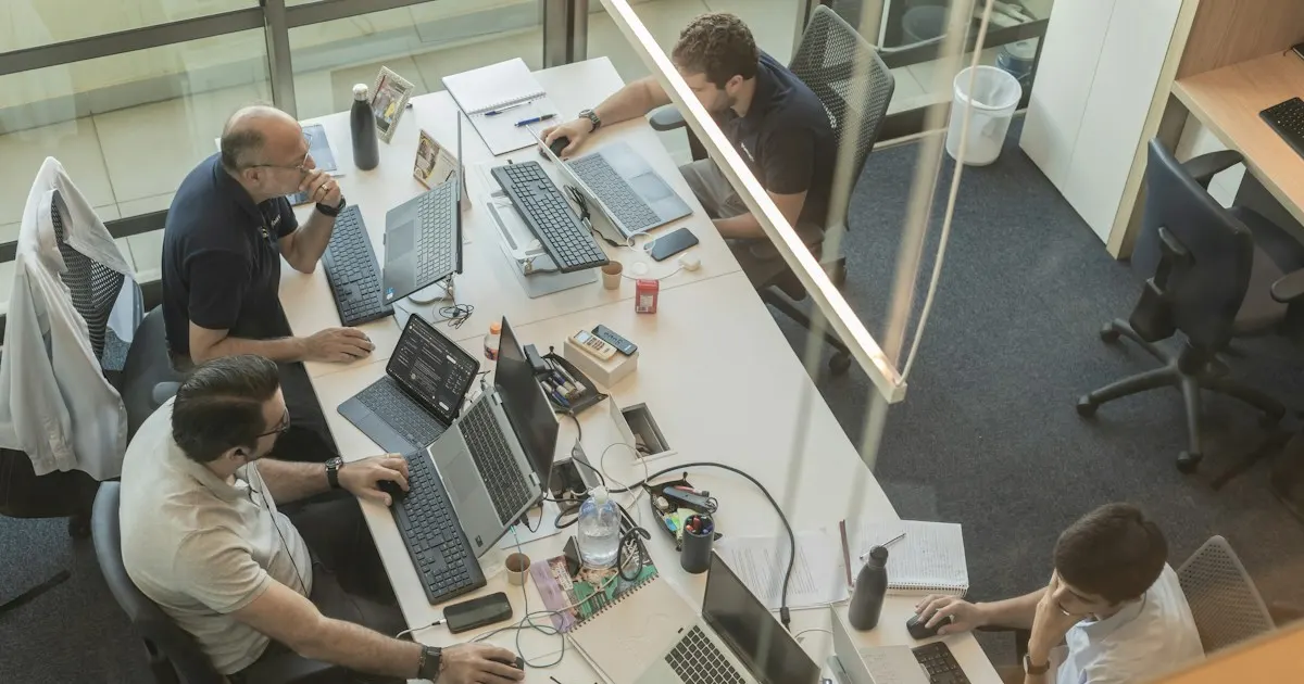 Overhead view of a team working together at a shared desk with multiple laptops