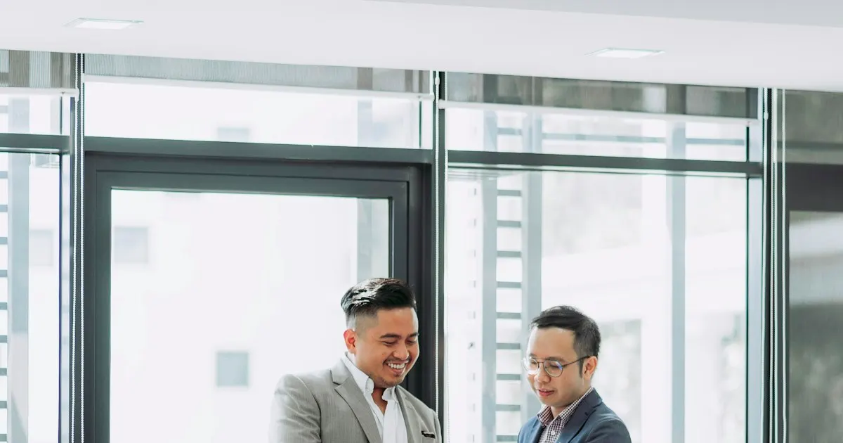 Two businessmen smiling while looking at a phone in a bright office