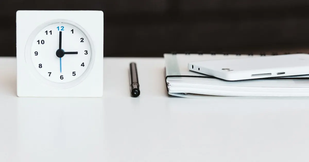 White desk clock next to a pen and notepad