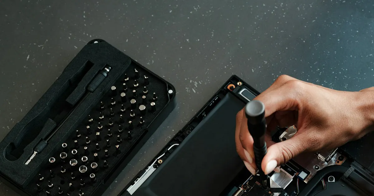 Close-up of hands repairing the internal components of an open laptop with a screwdriver