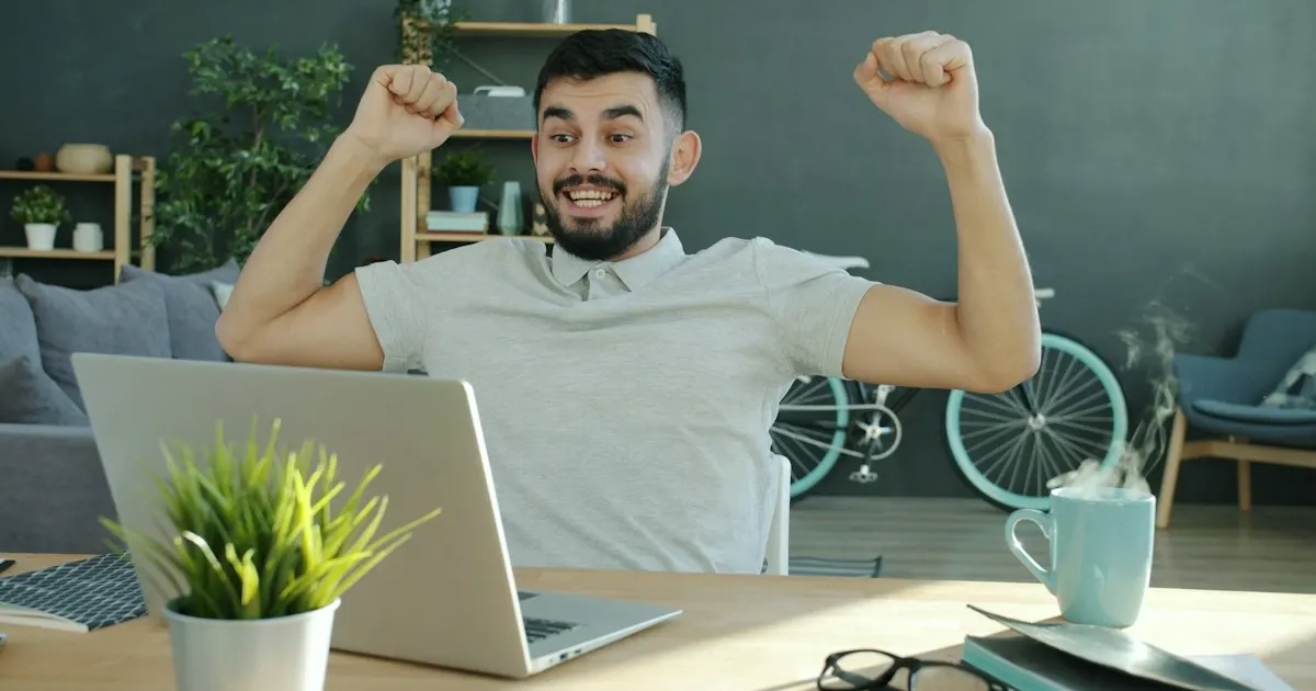 A man celebrating a win with raised fists while sitting at his laptop
