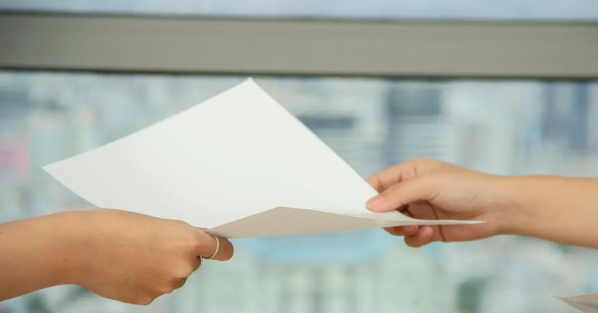 One person handing a document to another across a desk
